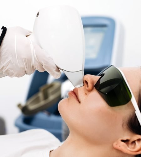 Woman receiving laser hair removal treatment while wearing protective eyewear in a clinical environment, medical device and equipment in the background